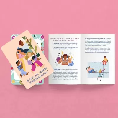 Cartas ilustradas e livreto aberto com texto em português sobre emoções numa mesa rosa