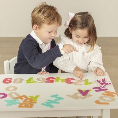 Crianças a brincar com letras e números de madeira coloridos numa mesa branca