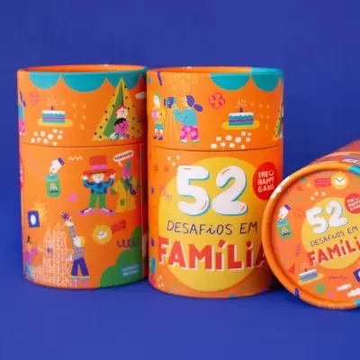 Embalagens cilíndricas laranja com texto e ilustrações infantis para jogo 52 Desafios em Família