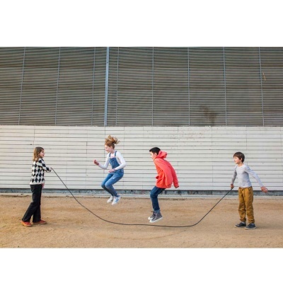 Quatro crianças brincam com corda de saltar ao ar livre junto a uma parede cinza.