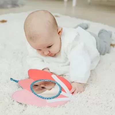 Brainquedo colorido com espelho para bebé sobre tapete branco, bebé de barriga para baixo