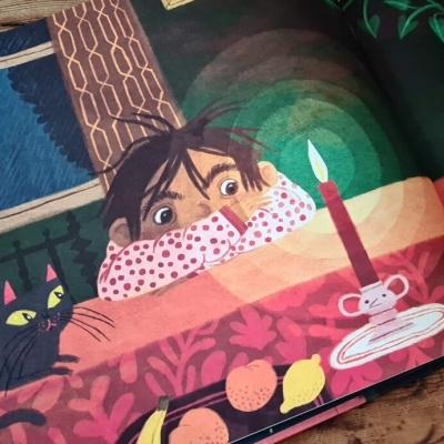 Livro ilustrado com criança, gato preto e vela acesa sobre mesa de madeira