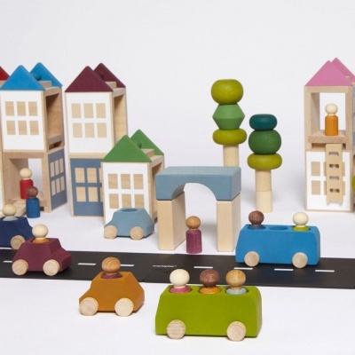 Brinquedos de madeira coloridos representando casas, árvores e carros sobre superfície branca com estrada preta