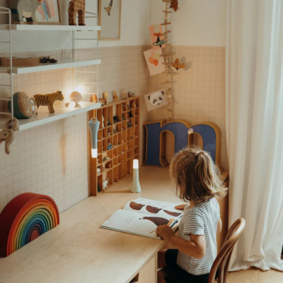 Criança sentada a ler num escritório infantil com decoração em madeira e objetos coloridos.