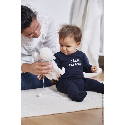 Bebé com pijama azul escuro e ursinho branco sentado no tapete com mulher