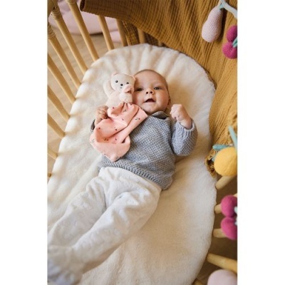 Bebé deitado num berço com almofada branca e brinquedo de peluche rosa