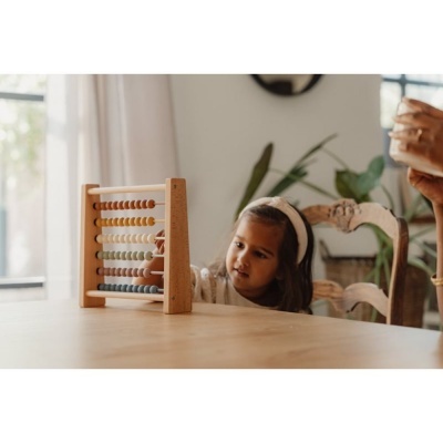 Ábaco de madeira com contas coloridas sobre mesa, criança ao fundo