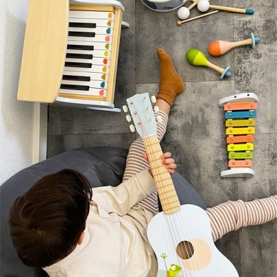Criança a tocar ukulele com vários instrumentos musicais de brinquedo ao redor