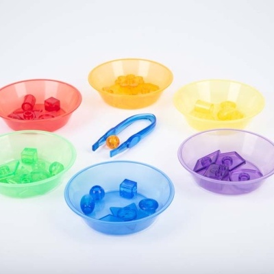 Seis tigelas coloridas com peças de plástico e uma pinça azul sobre fundo branco