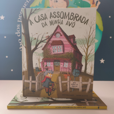 Capa do livro infantil A Casa Assombrada da Minha Avó com casa cor de rosa e criança de bicicleta.