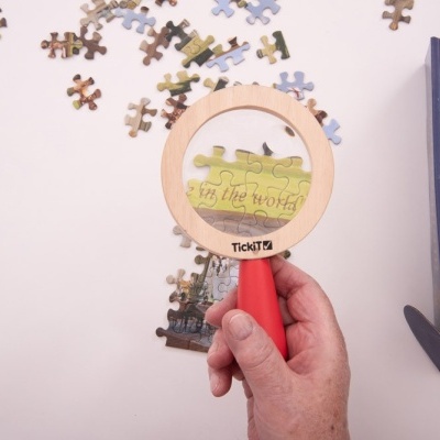 Lupa de madeira com pega vermelha sobre puzzle e caixa azul ao lado