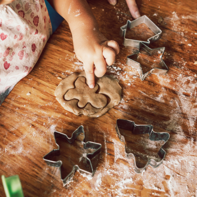 Criança a modelar massa para bolachas com formas metálicas de cortar numa mesa de madeira.