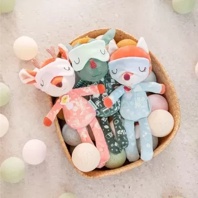 Três bonecos de peluche coloridos em cesta, rodeados por bolas decorativas pastel