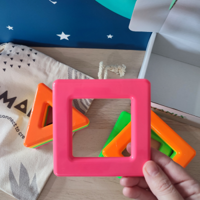 Brinquedos magnéticos coloridos quadrados e triângulos sobre superfície de madeira com saco de tecido e texto