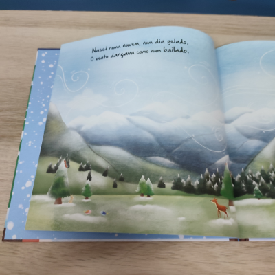 Livro infantil aberto com ilustração de montanhas e texto em português