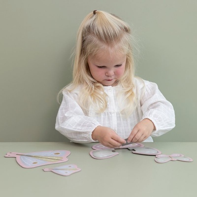 Menina loira a montar puzzle de madeira colorido numa mesa verde com fundo verde