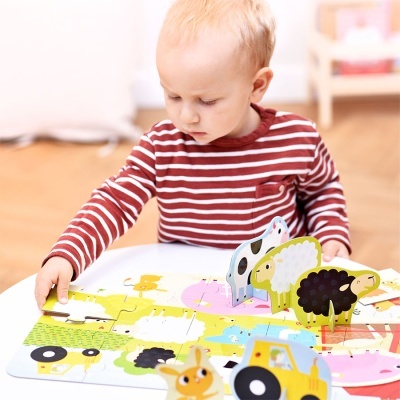 Criança loira a brincar com puzzle de madeira colorido de animais sobre mesa branca