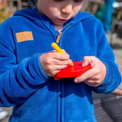Menino com casaco azul desenhando num bloco de notas vermelho em forma de coração