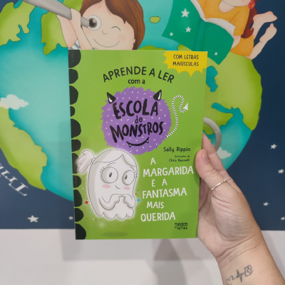 Livro infantil verde 'APRENDE A LER com a ESCOLA de MONSTROS' segurado por uma mão.