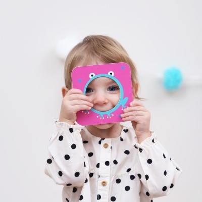 Menina pequena com camisa branca de bolinhas pretas segurando moldura de monstro rosa e azul