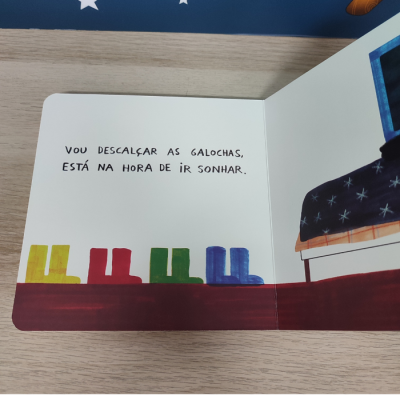 Página de livro infantil com texto e desenhos de galochas coloridas e cama com colcha de estrelas