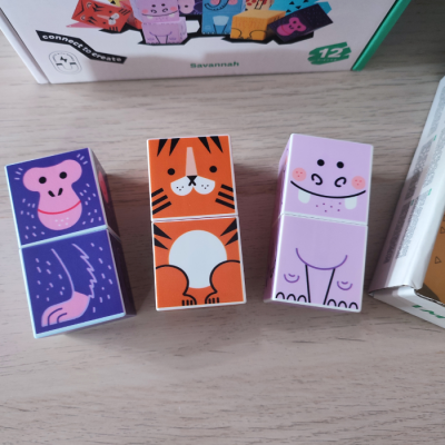 Blocos de madeira coloridos com desenhos de animais, macaco roxo, tigre laranja e hipopótamo lilás, sobre mesa de madeira clara.