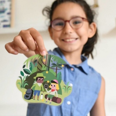 Criança com óculos segurando cartão ilustrado com pessoas na floresta