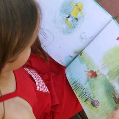 Criança a ler livro ilustrado ao ar livre com vestido vermelho