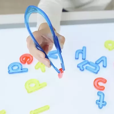 Letras de plástico coloridas e pinça azul numa mesa branca