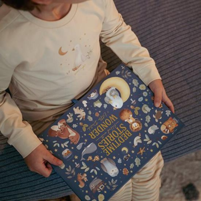 Criança com pijama creme segura livro infantil azul com ilustrações de animais