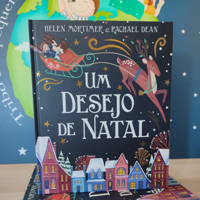 Capa de livro infantil UM DESEJO DE NATAL com ilustração de rena, trenó e casas coloridas