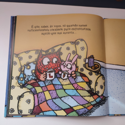 Livro infantil aberto com ilustração de coruja e coelho num sofá e texto em português