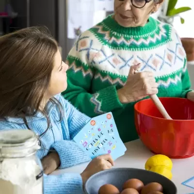 Duas pessoas a cozinhar numa cozinha, criança e idosa com camisolas tricotadas coloridas