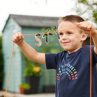 Menino a segurar fio com letras de madeira, casa de jardim ao fundo