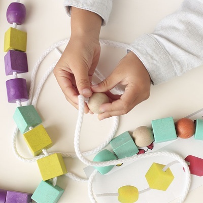 Criança a enfiar contas de madeira coloridas em fio