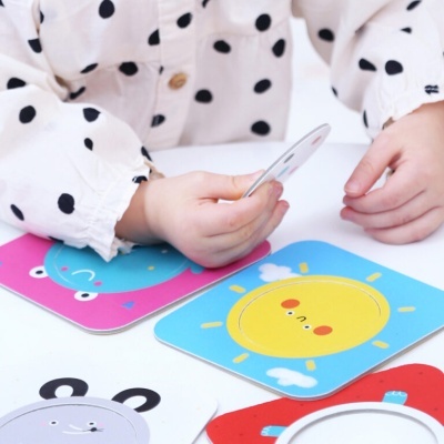 Cartões infantis coloridos com desenhos de sol, elefante e girafa nas mãos de uma criança com camisa de bolinhas pretas