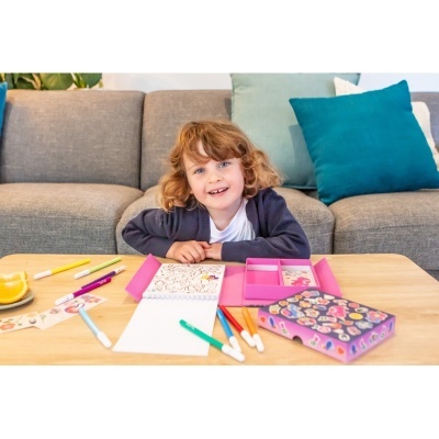 Criança sentada no sofá com material de desenho e colorir numa mesa à frente.