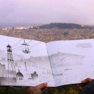 Homem a ler livro ilustrado em ambiente exterior com vista para cidade ao pôr do sol