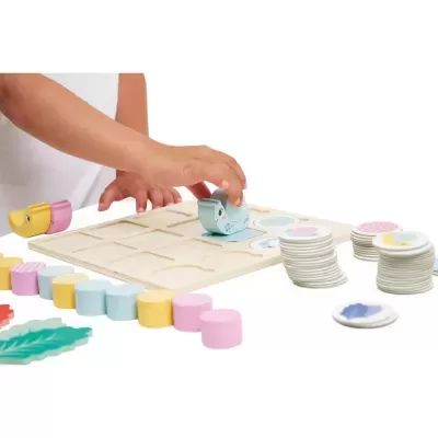 Jogo de tabuleiro de madeira com peças coloridas em tons pastel e folhas verdes decorativas.