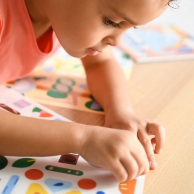 Criança a brincar com peças coloridas em cartolina numa mesa de madeira