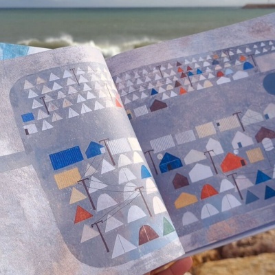Livro aberto com ilustrações geométricas coloridas junto ao mar e pedras