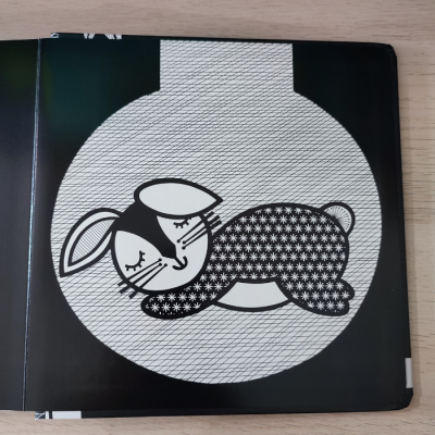 Ilustração em preto e branco de coelho num livro infantil aberto sobre mesa de madeira clara