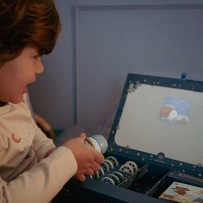 Criança com diapasão junto a caixa azul escura com acessórios e projeção infantil