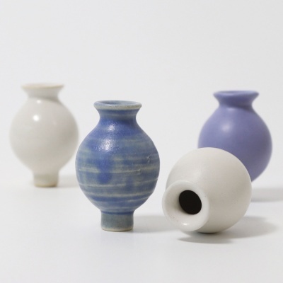 Quatro pequenos vasos de cerâmica em branco, azul e roxo sobre fundo branco