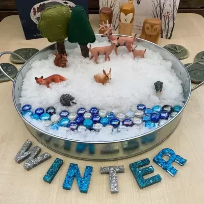 Tabuleiro com decoração de inverno com animais e árvores sobre tecido branco que simula neve