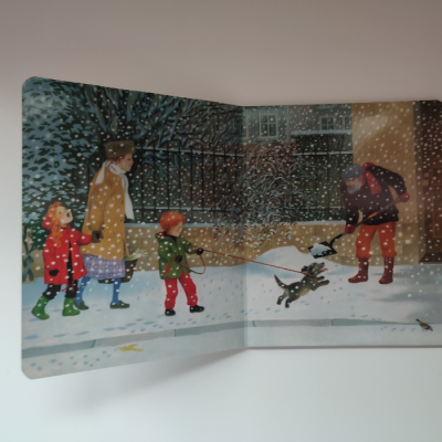 Livro infantil aberto com ilustração de família e cão na neve