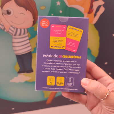 Caixa roxa do jogo VERDADE OU CONSEQUÊNCIA com texto e ícones, mão segurando e fundo com desenho infantil