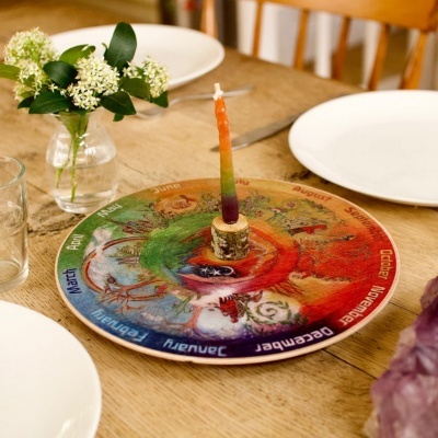 Tabuleiro do zodíaco colorido com vela no centro sobre mesa de madeira com pratos e flores