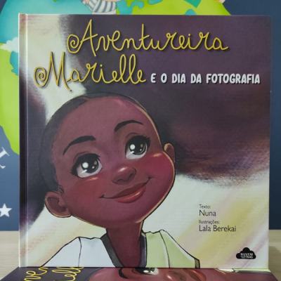 Capa de livro infantil 'Aventureira Marielle e o Dia da Fotografia' com ilustração de uma criança sorridente.