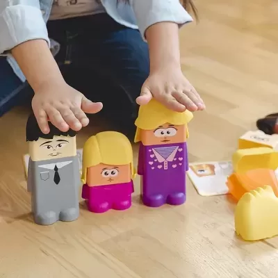 Brinquedos tipo bonecos coloridos com cabelos amarelos no chão de madeira e mãos de criança a tocar